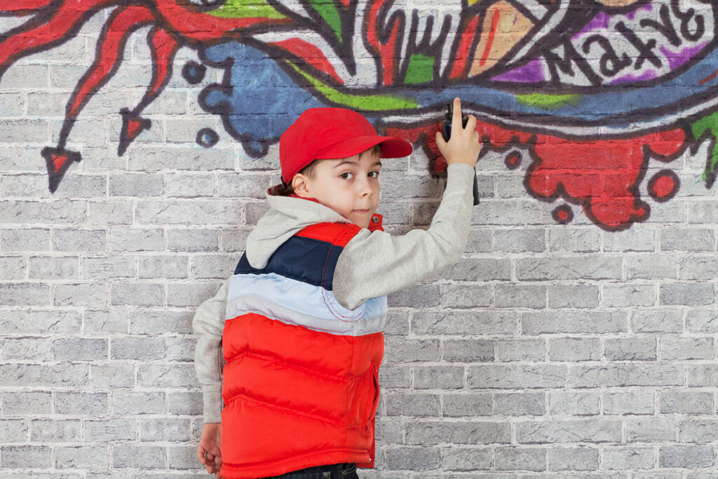 Ein Kind sprayt Grafitti an eine Ziegelwand
