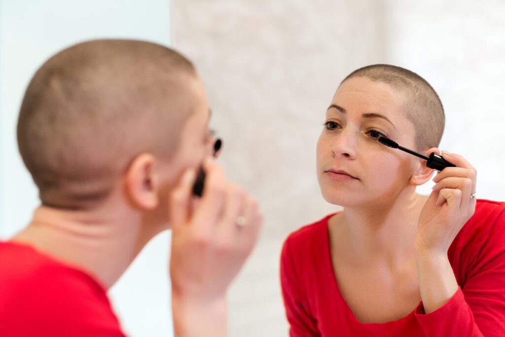 Junge krebskranke Frau schminkt sich beim Blick in den Spiegel