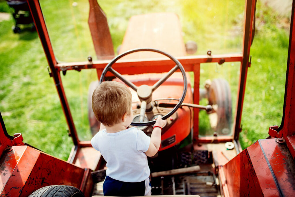 Kind sitzt in einem Traktor und hält das Lenkrad